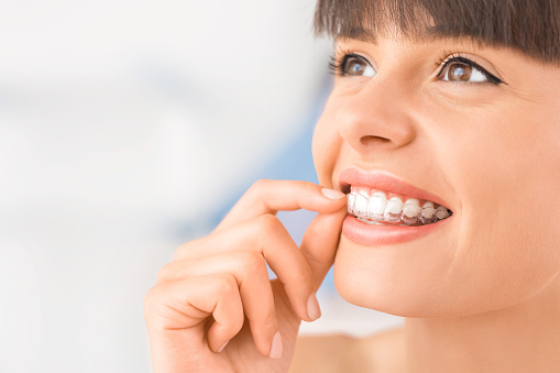 A woman smiling while putting in her Invisalign at D.A. Dental in Auburn, MA