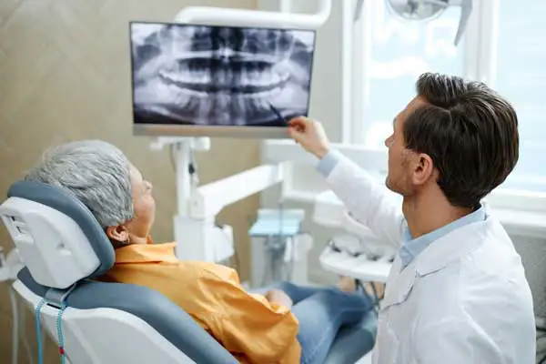 Back view of male dentist pointing at tooth X-ray image on screen during root canal consultation at D.A. Dental in Auburn, MA