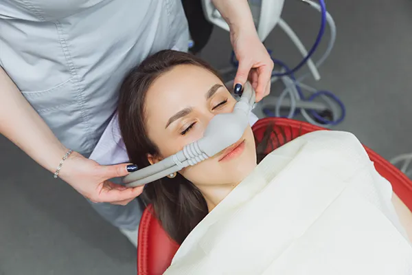Dental assistant fitting a sedation mask over the nose of her calm female patient at D.A. Dental in Auburn, MA