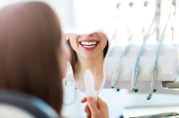 Woman looking at her smile in a mirror after getting dental restoration at D.A. Dental in Auburn, MA