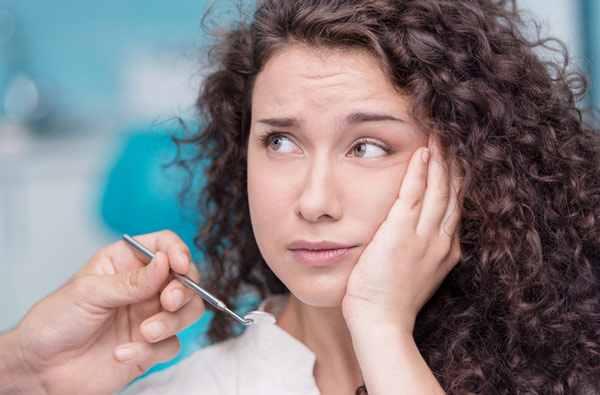Woman holding cheek in pain before tooth extraction at DA Dental in Auburn, MA