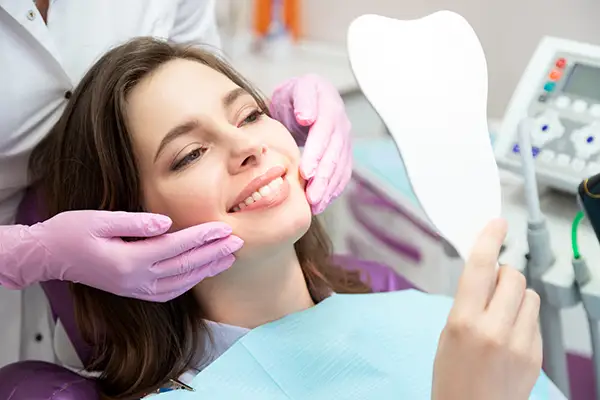 A smiling woman holding a tooth-shaped mirror with same day crowns at D.A. Dental in Auburn, MA