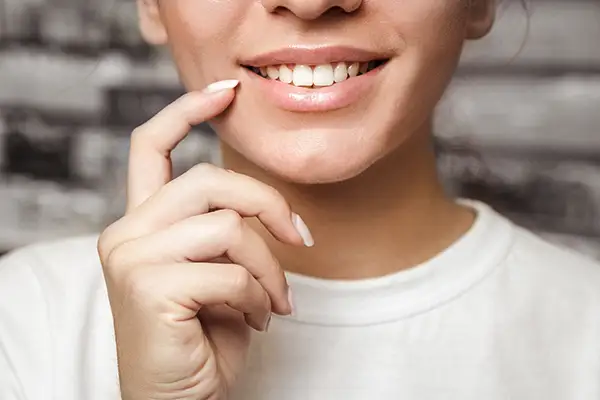 A close-up of a woman's smile with dental implants as she gently touches her teeth with her finger at D.A. Dental in Auburn, MA