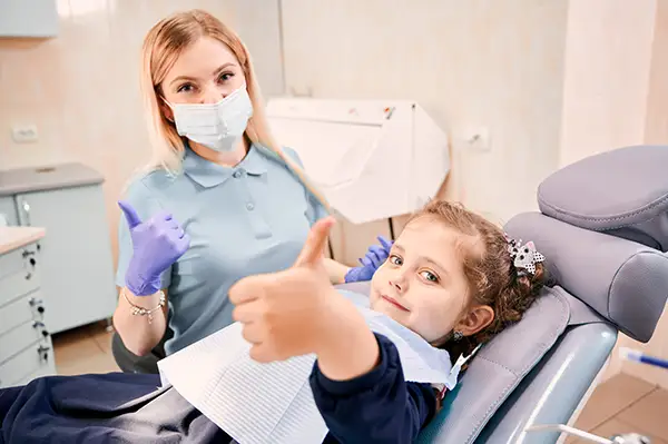 A happy little girl and a masked dental hygienist giving a thumbs up together at D.A. Dental in Auburn, MA