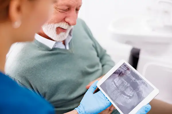A dental assistant showing a digital x-ray to a senior patient on a tablet at D.A. Dental in Auburn, MA